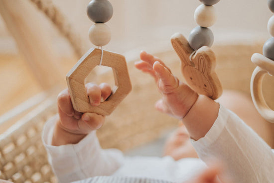 A baby reaching and grasping wooden hanging toys on a play gym, exploring hand-eye coordination and early motor development.