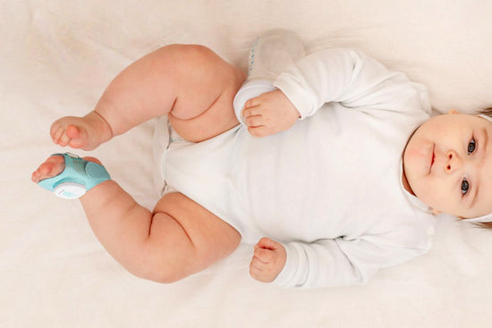 A baby lying on a soft blanket wearing a green Sense-U Sock Shoe baby monitor on their foot.