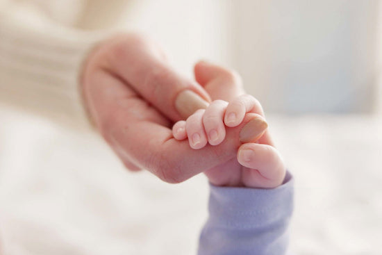 A newborn baby's tiny hand gently holding an adult's finger, captured in soft light to convey tenderness, trust, and care.