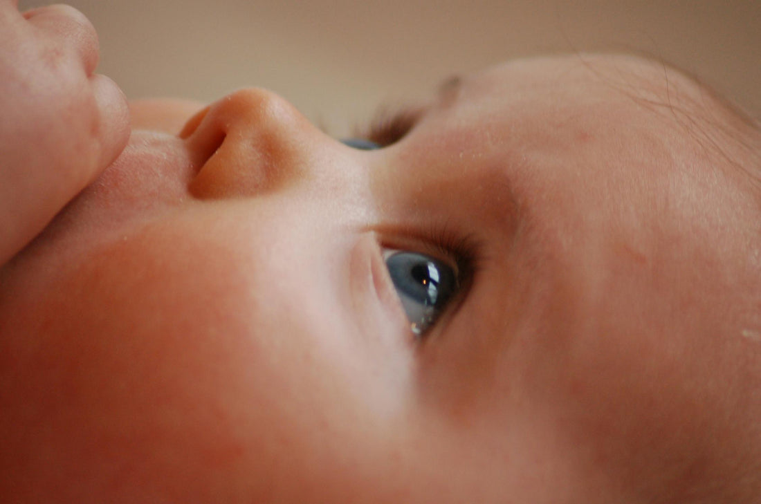 Close-up of a baby's face, gazing upwards with wide blue eyes. The image conveys innocence and wonder, with soft lighting highlighting the baby's features.