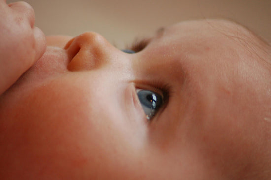 Close-up of a baby's face, gazing upwards with wide blue eyes. The image conveys innocence and wonder, with soft lighting highlighting the baby's features.