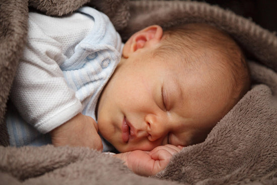 Sleeping newborn baby wrapped in a soft gray blanket, eyes closed and hands tucked near the face, conveying warmth, comfort, and peace.